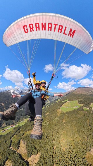 A person paragliding with a parachute labeled 'GRANATALM' over a mountainous landscape. 1