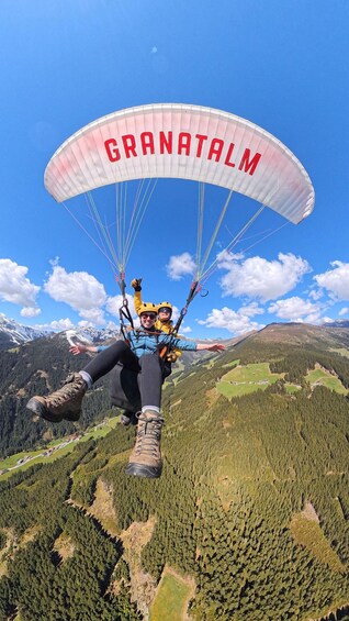 A person paragliding with a canopy labeled 'GRANATALM' over a mountainous landscape. 3