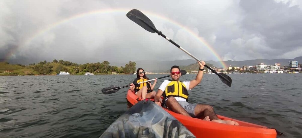 Two people kayaking on a body of water with a rainbow in the background. 3