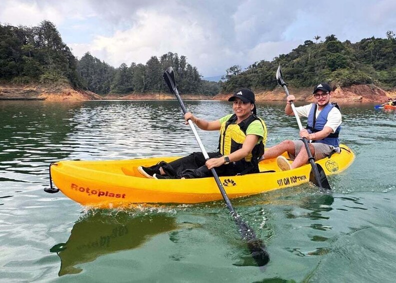 Two people in a yellow kayak on a calm body of water with trees and hills in the background. 2