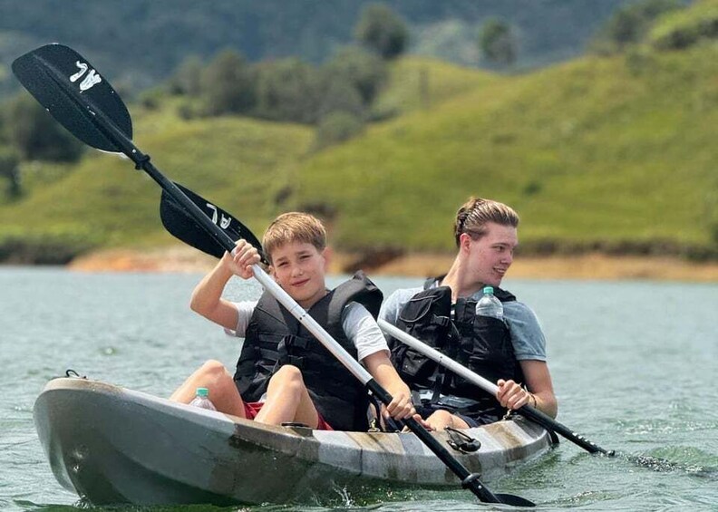 Two people in a small boat on a body of water with a green landscape in the background. 4