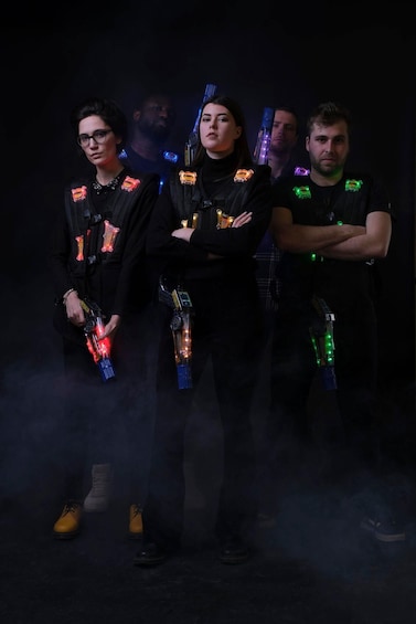 Four individuals standing with arms crossed, wearing black outfits with glowing wristbands and backpacks. 3