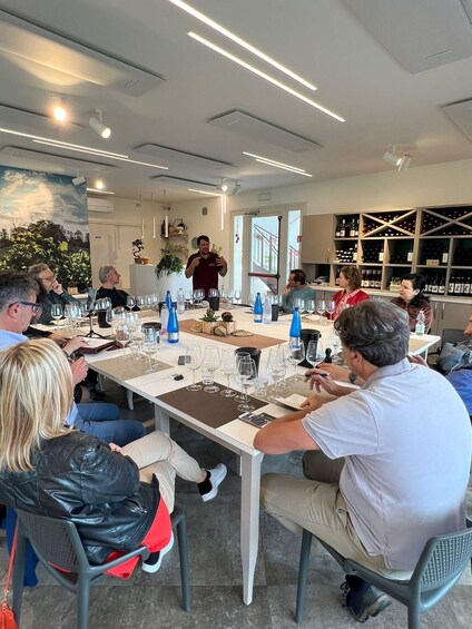 A group of people seated at a table with wine glasses and bottles, in a room with a modern interior and a wine rack in the background. 4