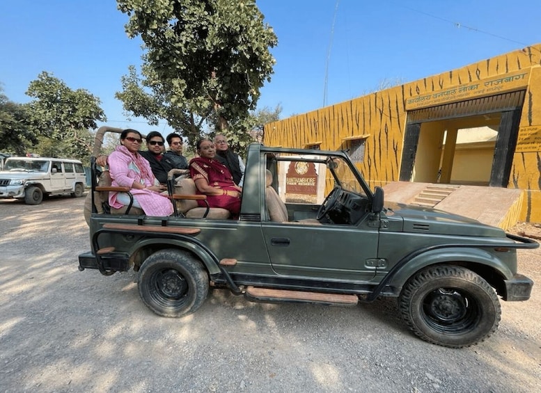 A green jeep with passengers, parked in front of a building with a sign that reads 'Panthambore.' 3