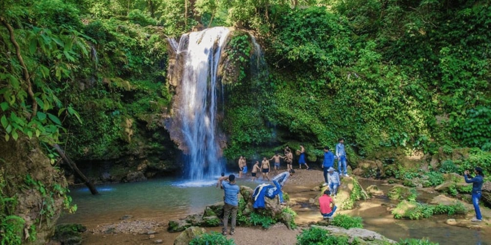 A waterfall in a lush forest with people around the water. 4
