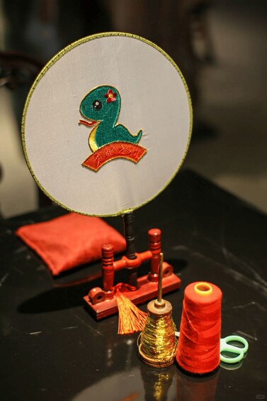 A sewing machine with a circular mirror, a red cushion, a spool of red thread, a spool of golden thread, and a pair of green scissors. 5
