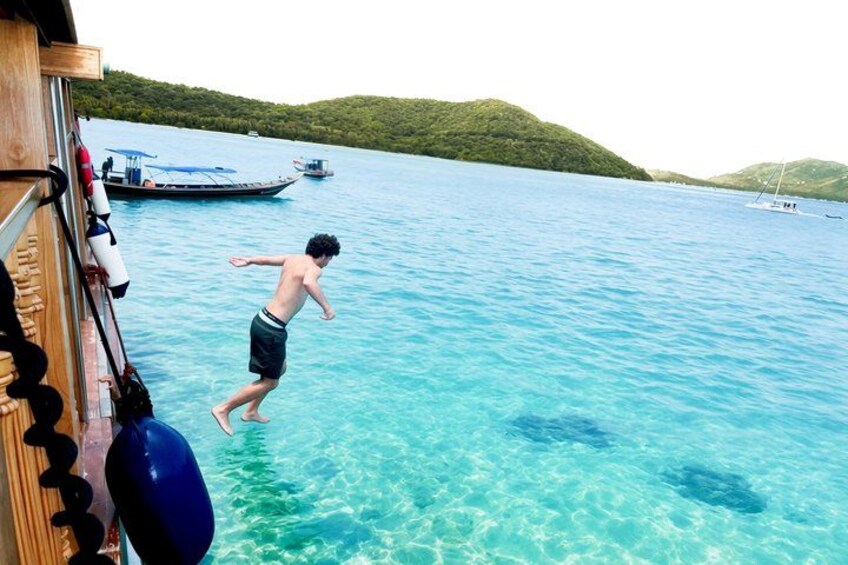 A person jumping into clear blue water from a dock, boats in the background, and green hills. 3