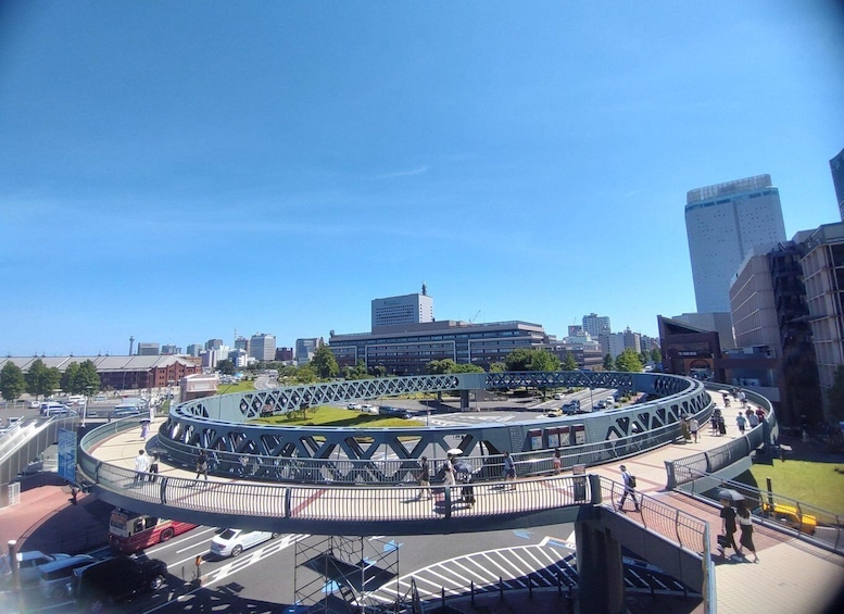 A circular pedestrian bridge with a metal lattice structure, surrounded by a cityscape with modern buildings and a clear blue sky. 4