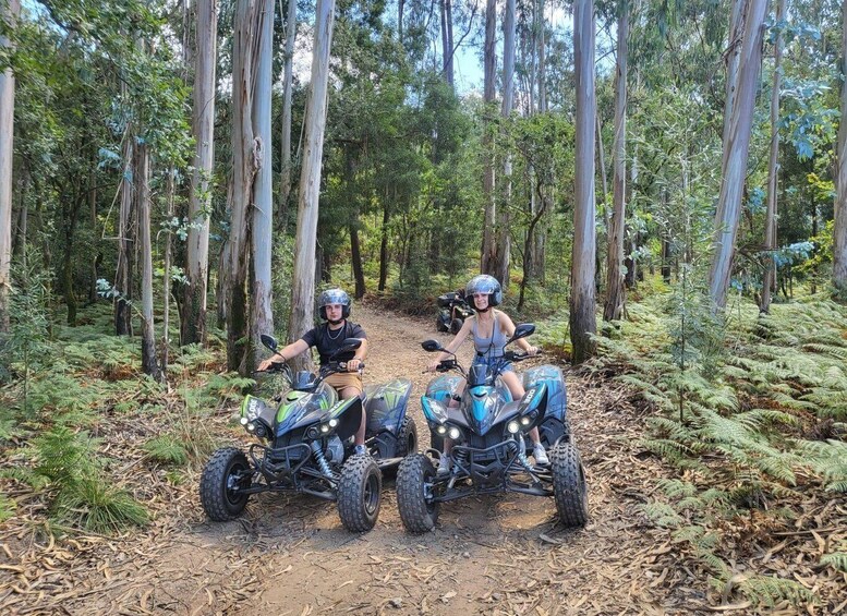 Two people riding all-terrain vehicles in a forest. 1
