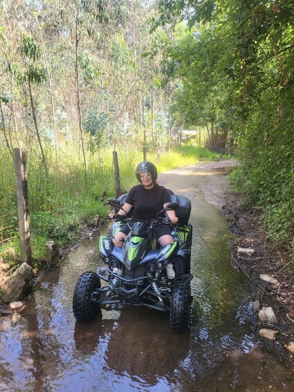 A person riding an ATV on a muddy path surrounded by greenery. 2