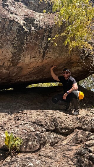 A person crouching under a large rock with a yellow hard hat and climbing gear. 4