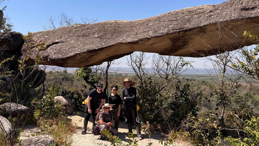 A group of people standing under a large rock formation with a desert landscape in the background. 5