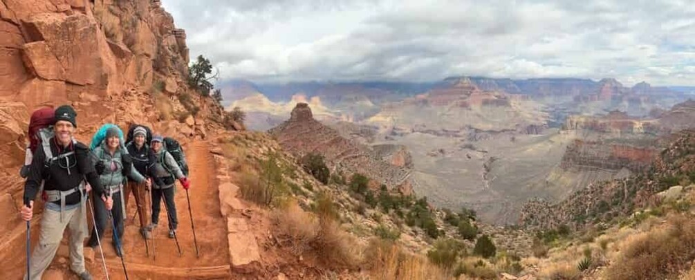 A group of hikers on a rocky trail with a canyon view in the background. 3