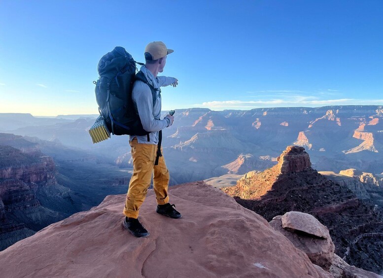 A person standing on a rock with a large backpack, overlooking a vast canyon landscape. 1