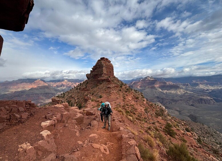 A hiker on a rocky trail with a view of the Grand Canyon in the background. 5