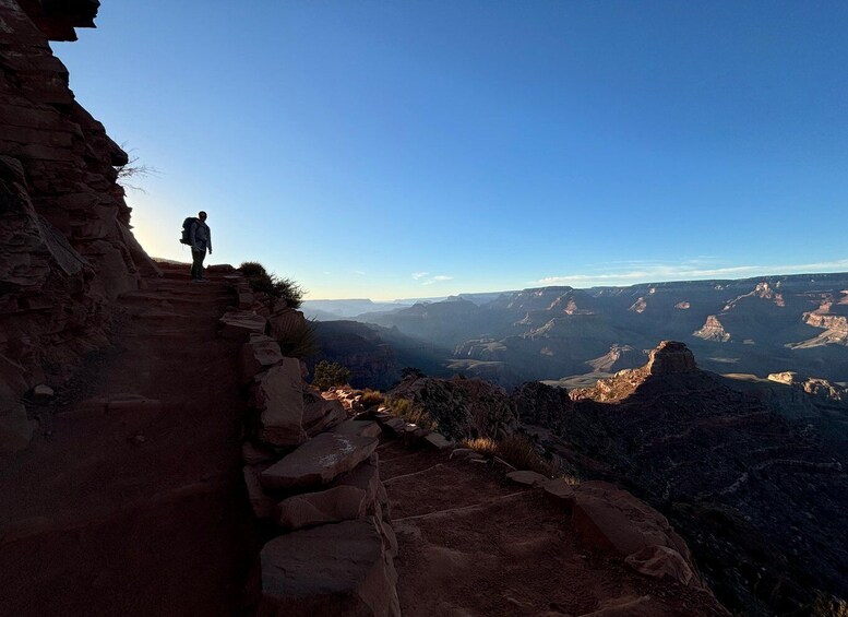A person hiking on a rocky trail with a vast canyon landscape in the background. 4