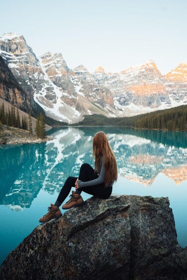 A person sitting on a rock by a calm lake with mountains in the background. 3