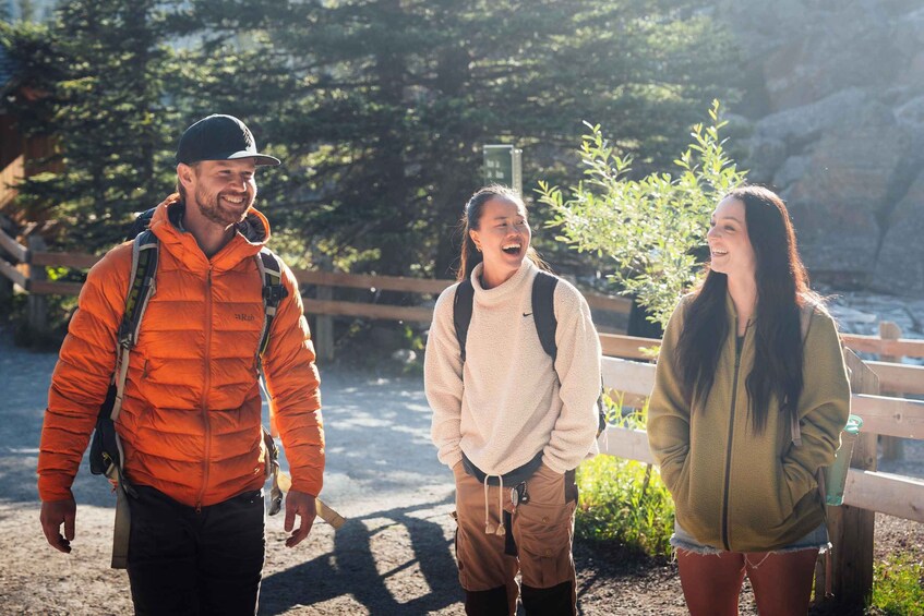 Three people hiking in a wooded area with a wooden fence and trees in the background. 2
