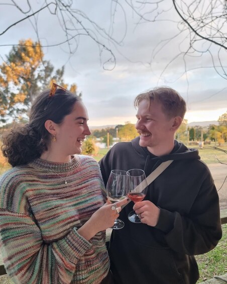 Two people holding wine glasses, standing outdoors with trees and a cloudy sky in the background. 5