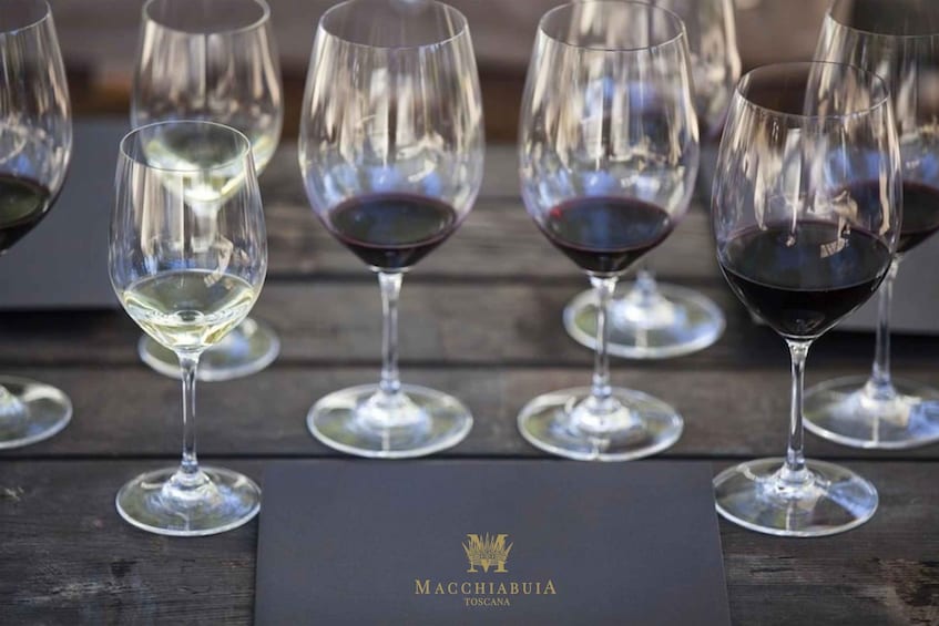 Wine glasses on a wooden surface with a logo of 'MACCHIABUIA TOSCANA' in the center. 4
