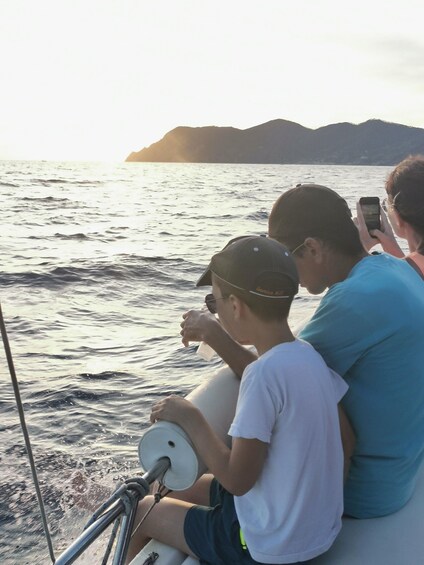 Three people on a boat, one holding a smartphone, another drinking from a cup, and the third looking at the water. 5