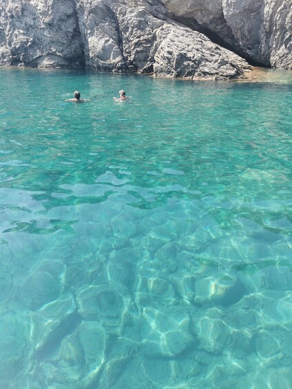 Clear turquoise water, rocky cliffs, and two people swimming. 3