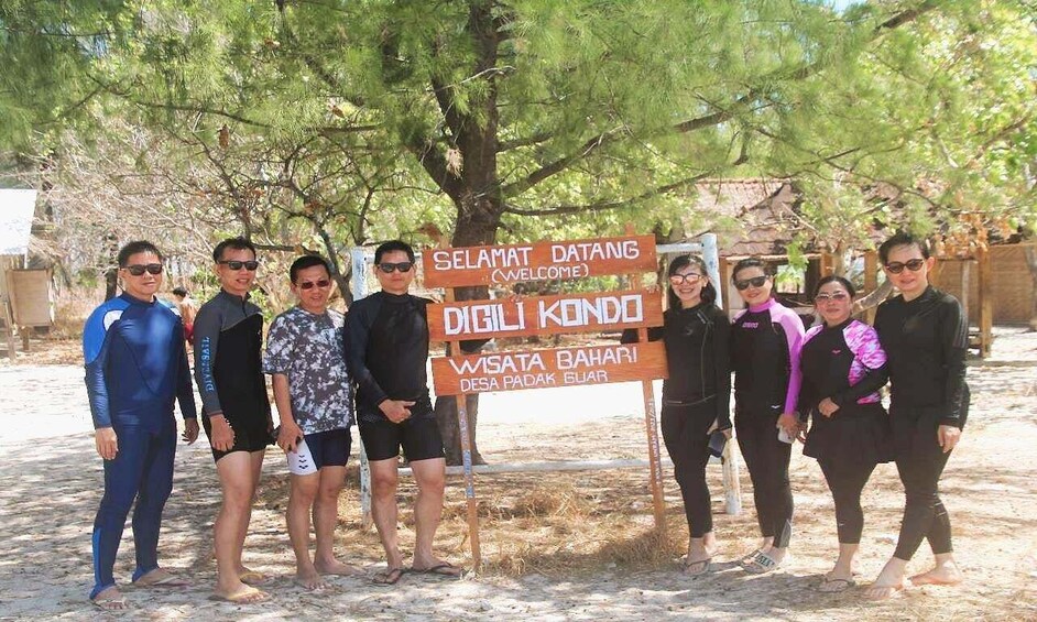 A group of people standing in a natural setting with a sign that reads 'Selamat Datang (Welcome)' and 'Digi Kendo Wisata Bahari Desa Padak Bulan.' 3