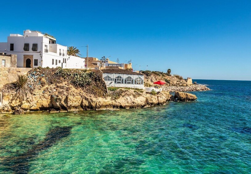 A coastal town with white buildings, clear blue sea, and rocky cliffs. 2