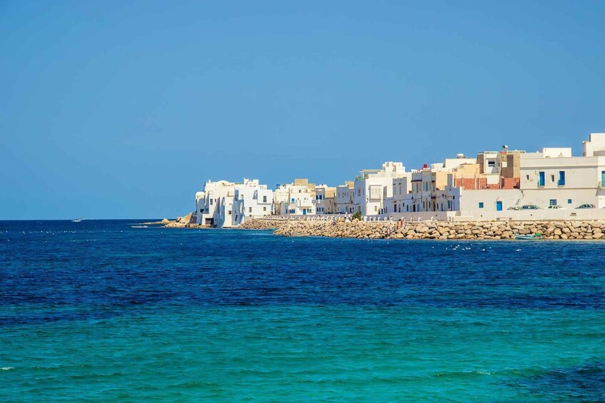 A coastal town with white buildings, a rocky breakwater, and the sea. 3