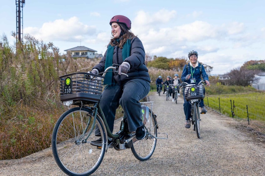 Two cyclists on a gravel path with numbered bike baskets, surrounded by vegetation and a clear sky. 1