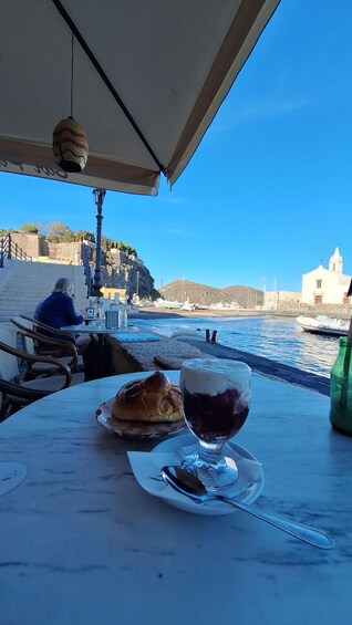 A table with a pastry and a glass of red wine, overlooking a coastal area with boats and a church. 3