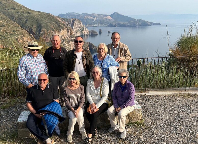 A group of people posing on a rocky outcrop with a coastal landscape in the background. 4