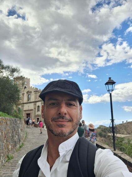 A man taking a selfie with a historic building and a stone wall in the background. 5