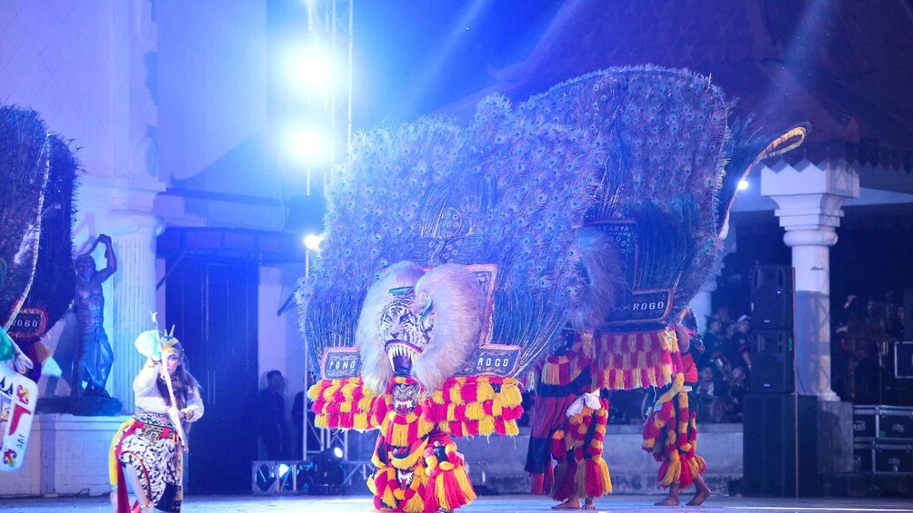 A cultural performance with performers in elaborate costumes and a large decorative headpiece. 1