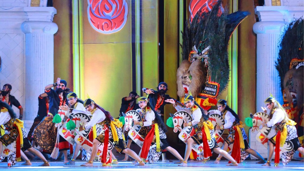 A group of performers in traditional costumes dancing on a stage with a large backdrop. 4