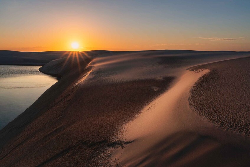 A desert landscape with a body of water and a sunset. 1
