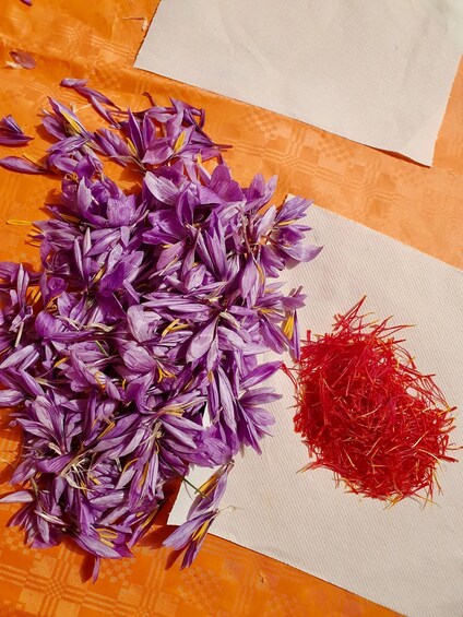 A pile of purple flowers and a pile of red shredded material on a textured orange surface. 4