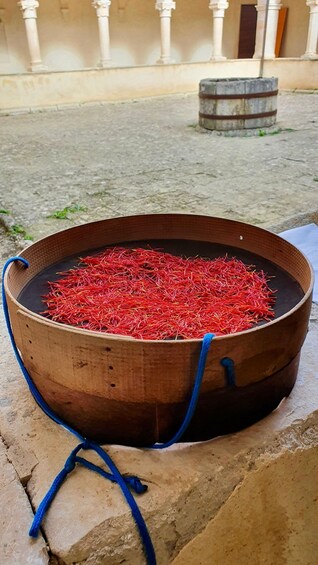 A large wooden basin filled with red fibers, possibly saffron, outdoors with a building and a barrel in the background. 5