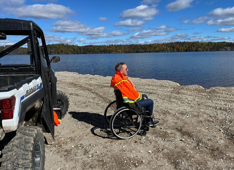 A person in a wheelchair by a vehicle with a rugged terrain and a lake in the background. 3