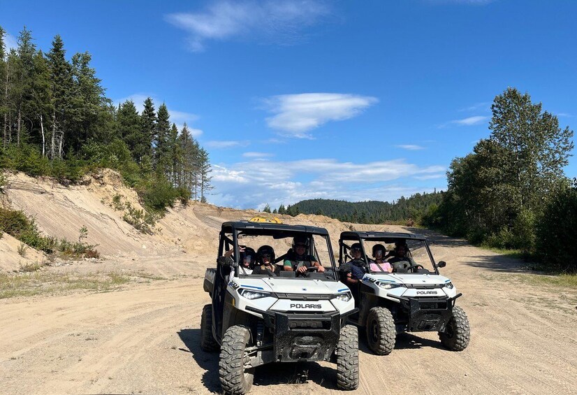 Two Polaris off-road vehicles on a dirt road with a forested landscape. 1