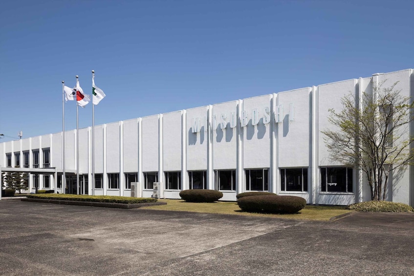 A modern building with a sign reading 'MITSUIROSHI'. There are two flags on flagpoles, and the building has a flat roof and large windows. 5