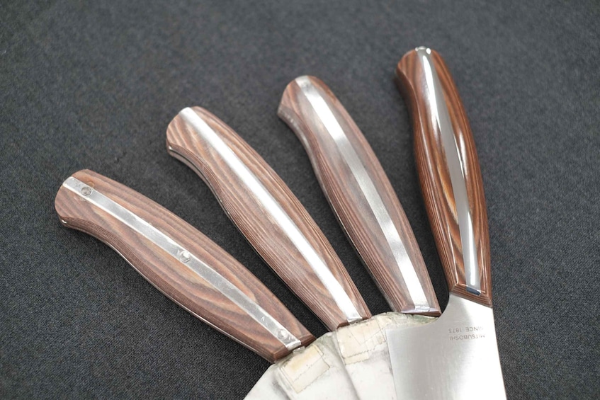 Four knives with wooden handles and metal blades, lying on a dark surface. 2