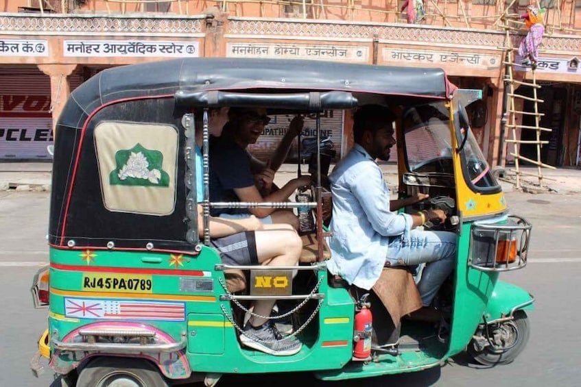 A green auto-rickshaw with passengers, parked on a street with buildings in the background. 3