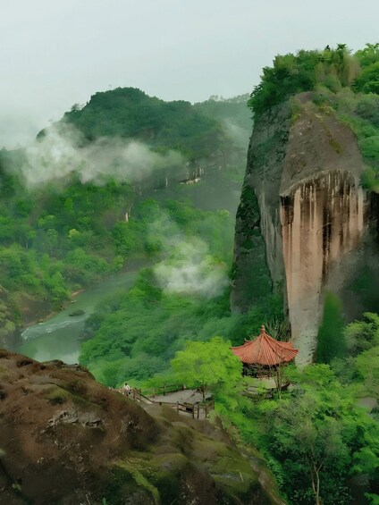 A temple nestled in a lush valley with a river, surrounded by dense greenery and a prominent rock formation. 2