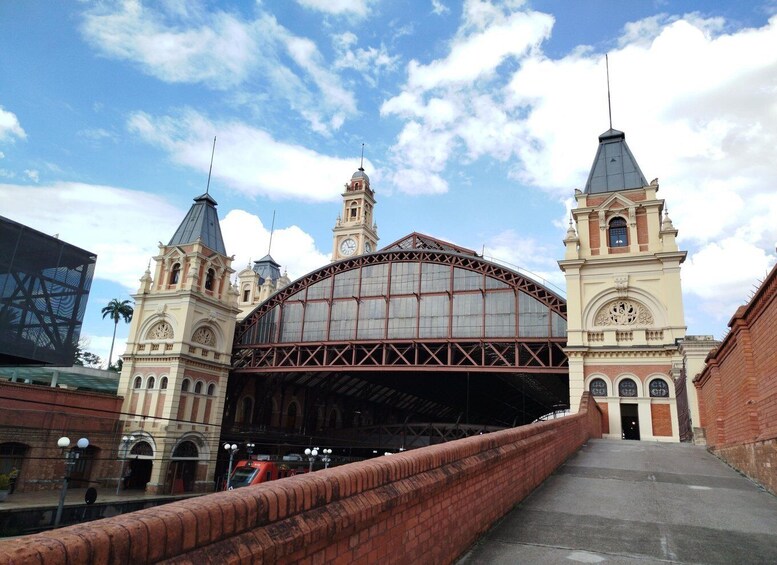 A historic train station with a large arched roof, two clock towers, and a modern building to the left. 1