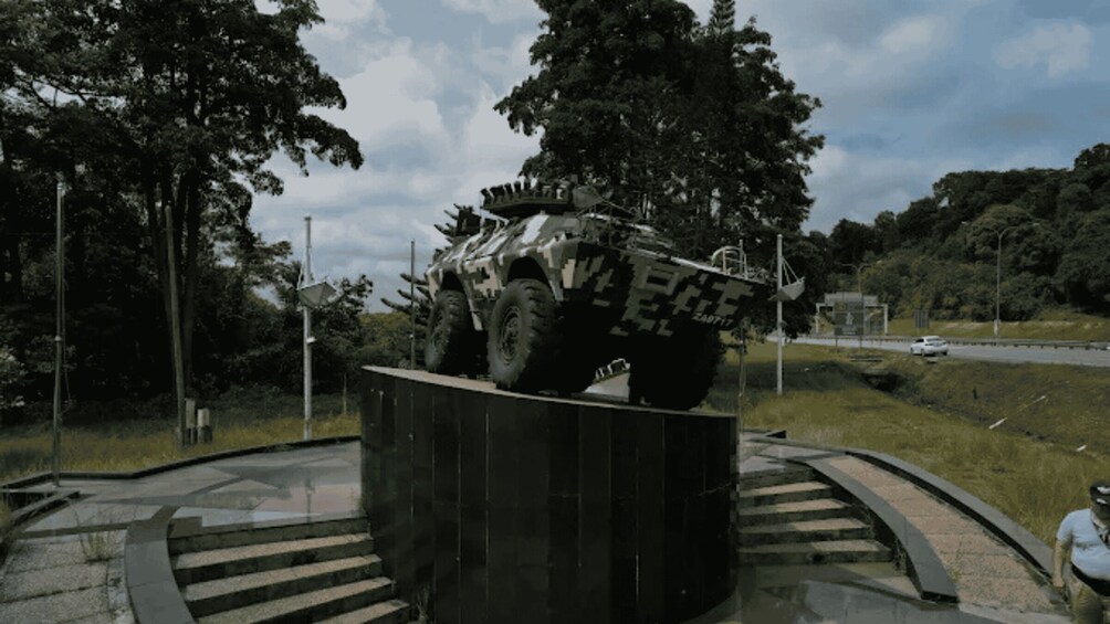 A large armored vehicle on display, surrounded by a circular platform with steps, trees, and a road in the background. 4