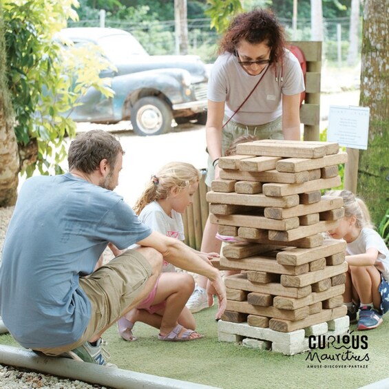 People playing a wooden block game outdoors with a car and greenery in the background. 4