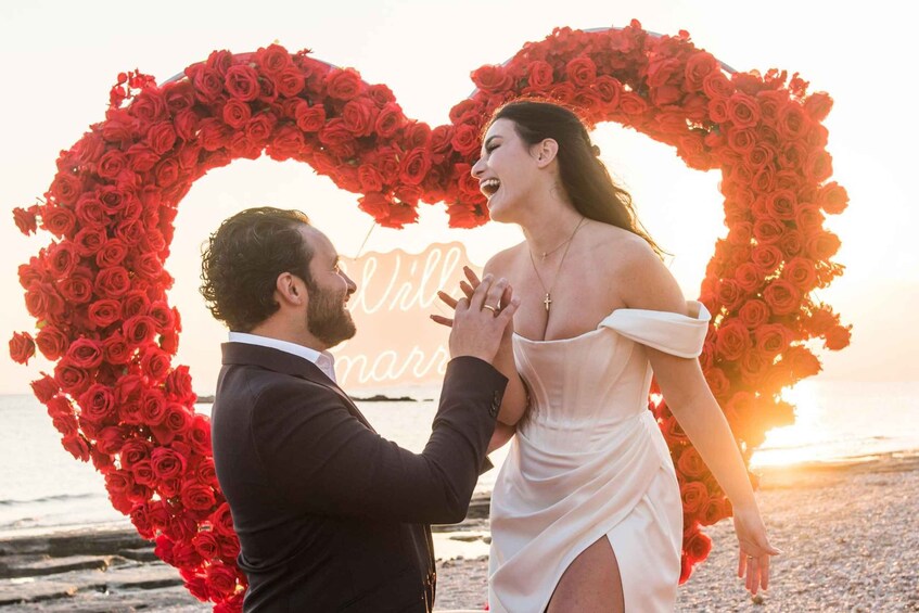 A couple embracing in front of a heart-shaped floral arrangement with a sunset in the background. 1