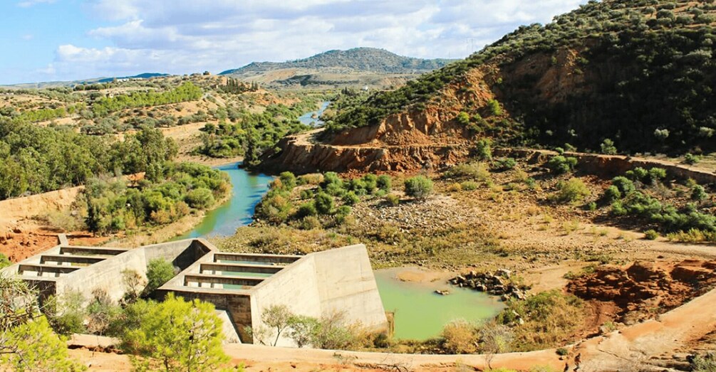A river flowing through a dry, hilly landscape with sparse vegetation and a few buildings near the water. 2