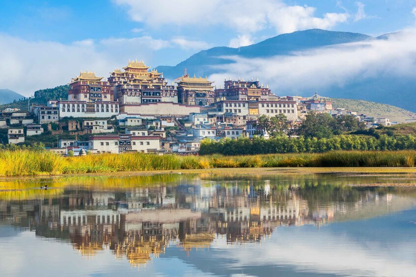 A traditional multi-tiered temple complex with intricate architecture, reflecting in a calm body of water, surrounded by lush greenery and mountains. 2